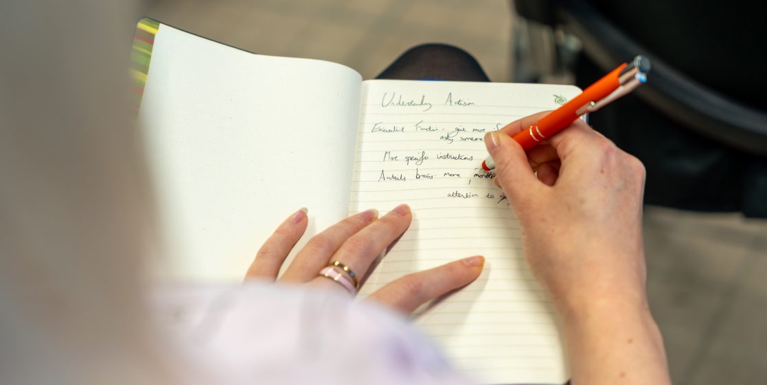 Over-the-shoulder shot of a woman taking notes during a neurodiversity training session
