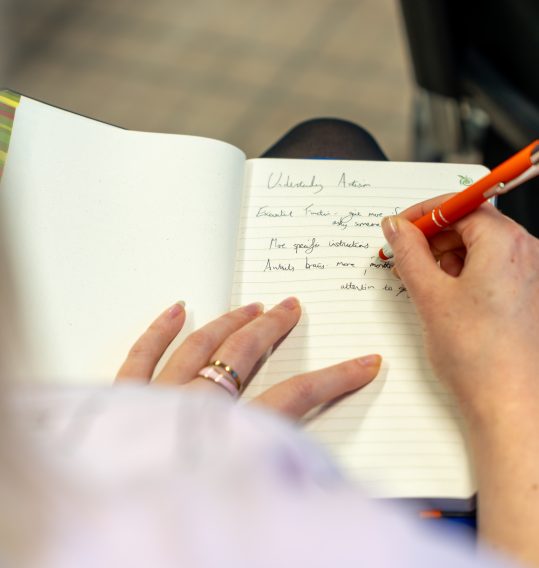 Over-the-shoulder shot of a woman taking notes during a neurodiversity training session